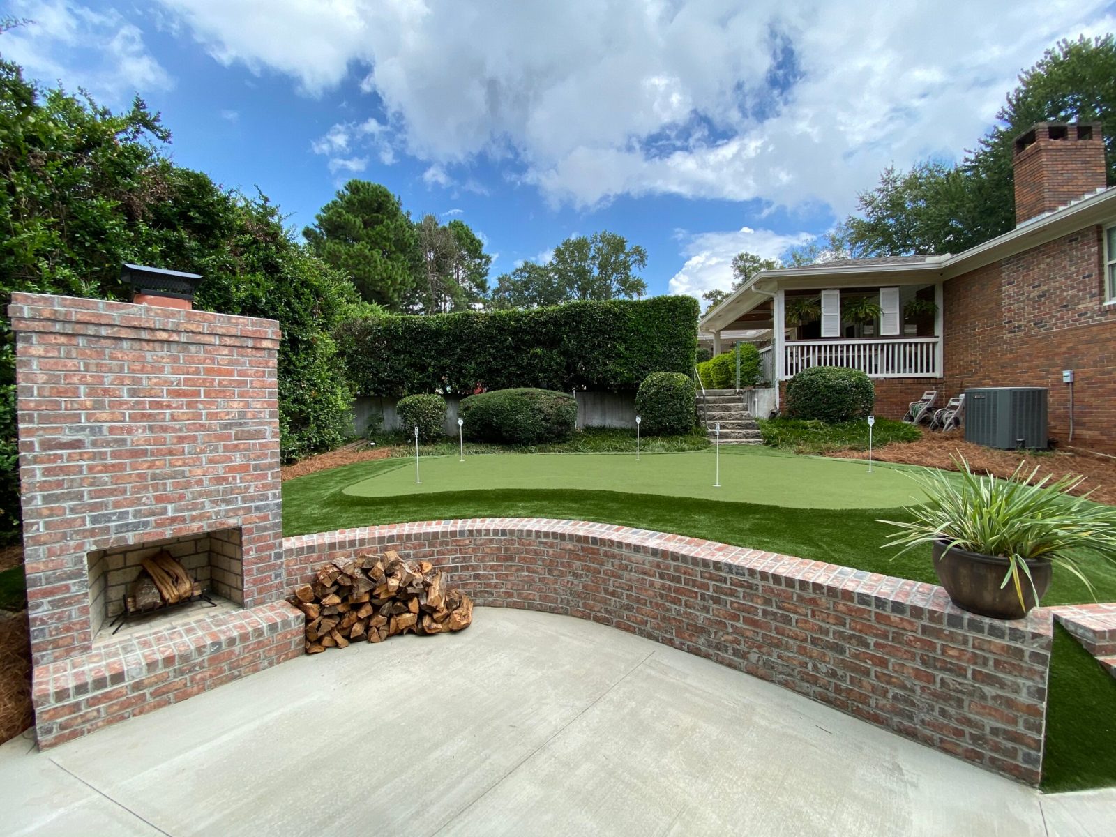 Brick outdoor fireplace and curved seat wall beside a backyard putting green in Augusta, Georgia