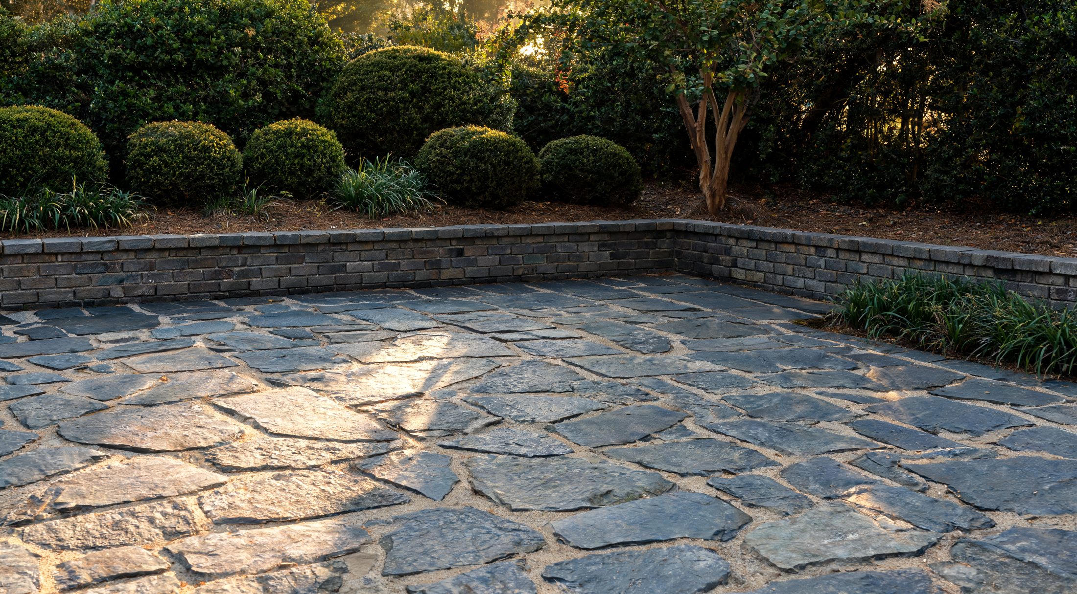 Bluestone flagstone patio enclosed by a low brick seat wall at golden hour