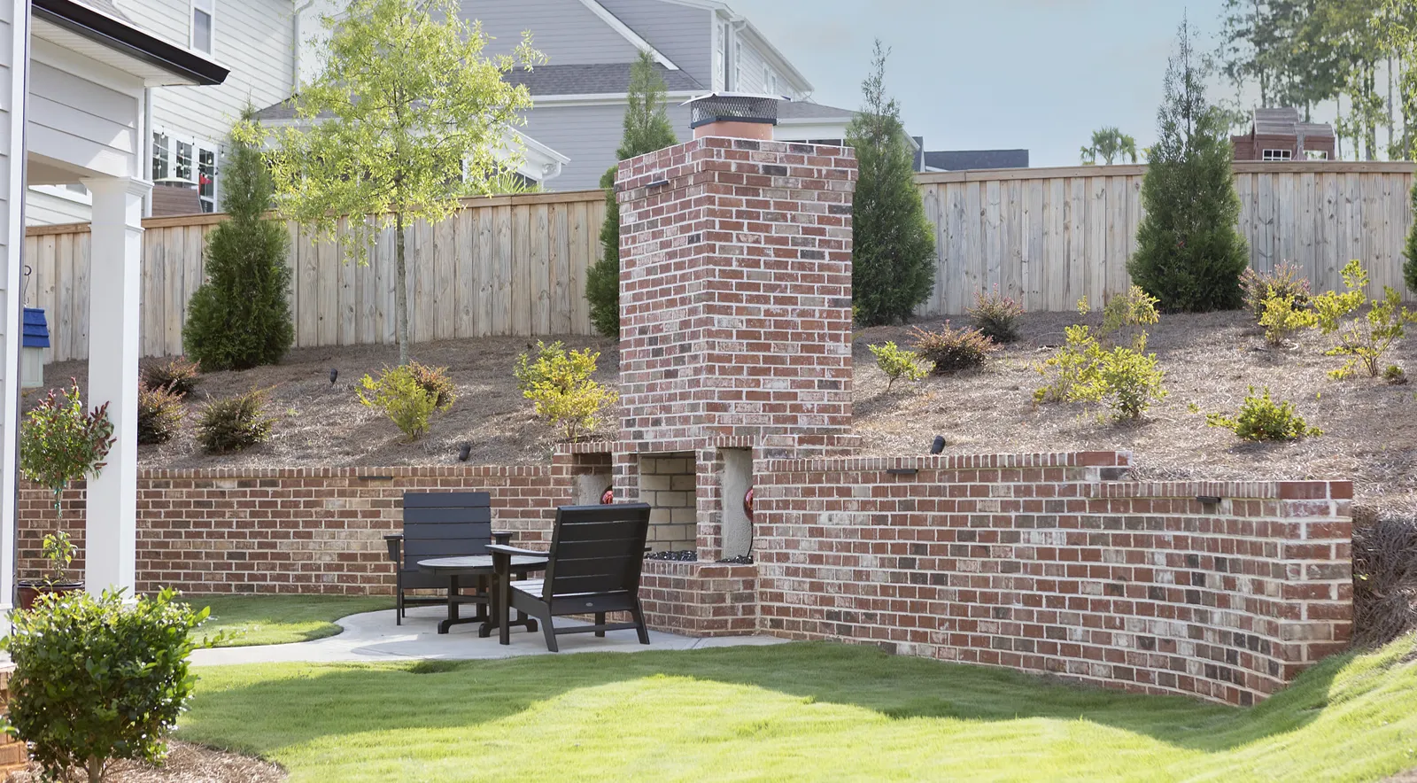 Brick outdoor fireplace built into a tiered brick seat wall below a freshly planted slope