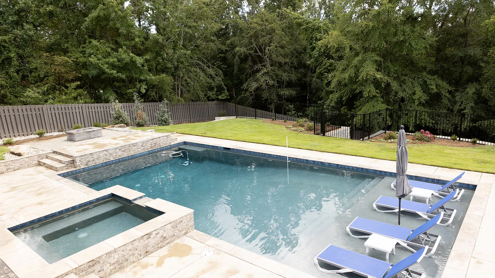 Rectangular pool and raised spa on a travertine deck with loungers and a folded umbrella