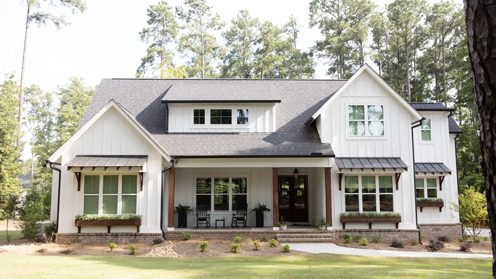 White board-and-batten farmhouse with cedar porch posts and planted window boxes above a wide mown lawn