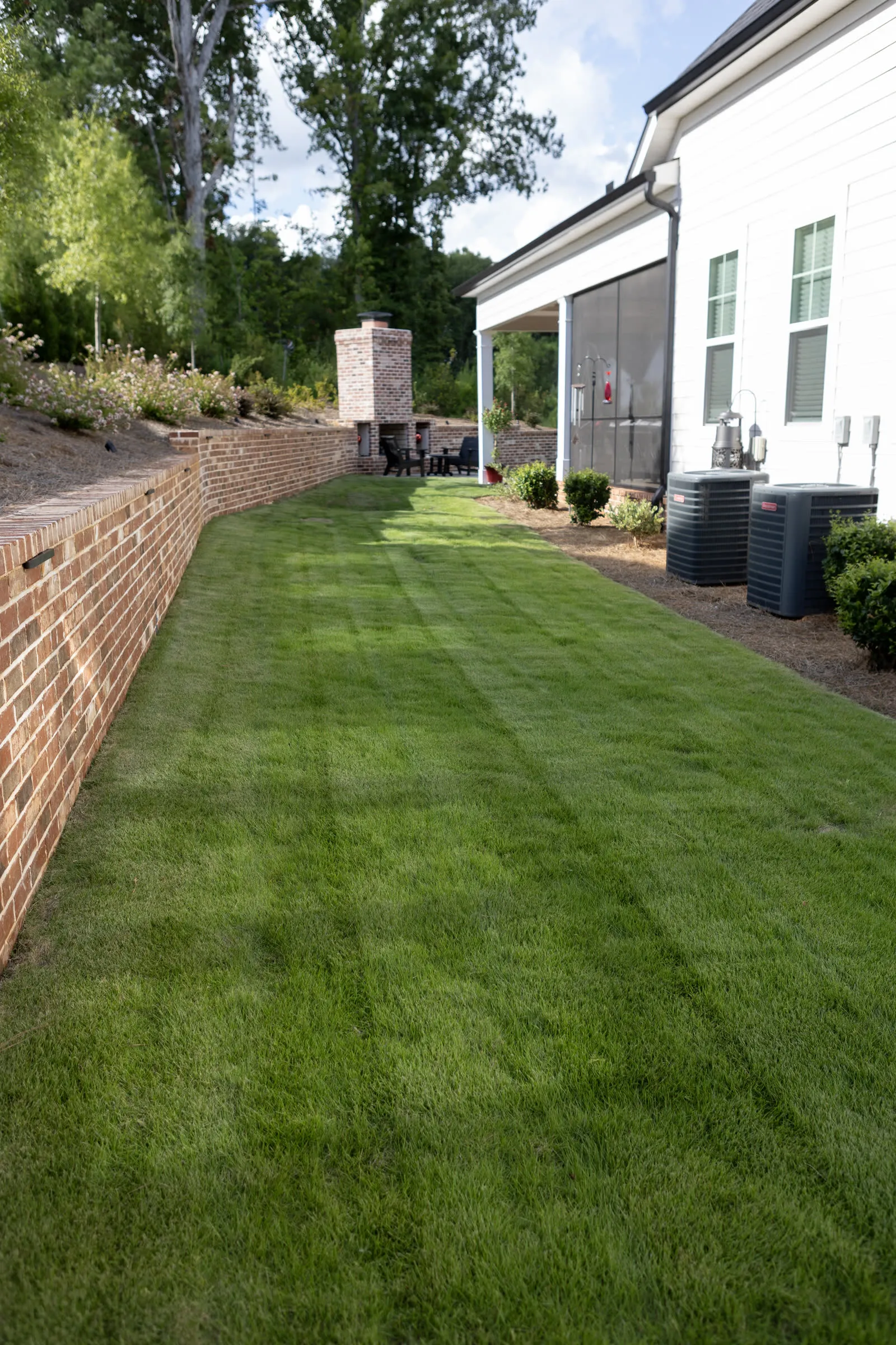 Lawn striped in even bands running between a brick retaining wall and the side of a home