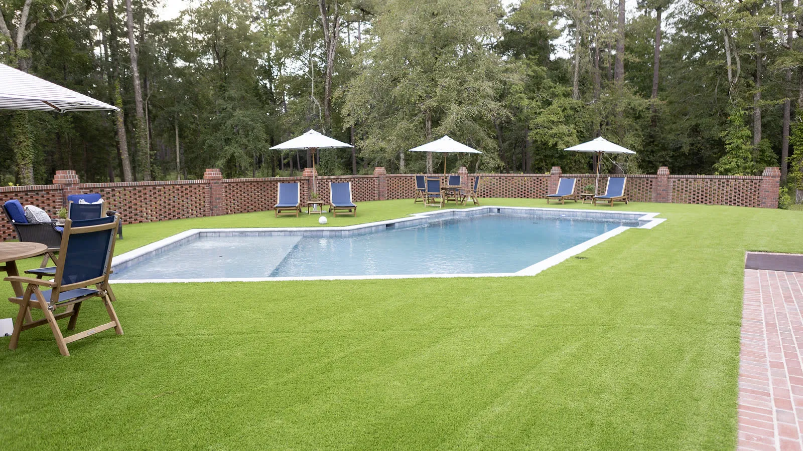 Dense, evenly striped lawn running up to a pool and brick garden wall