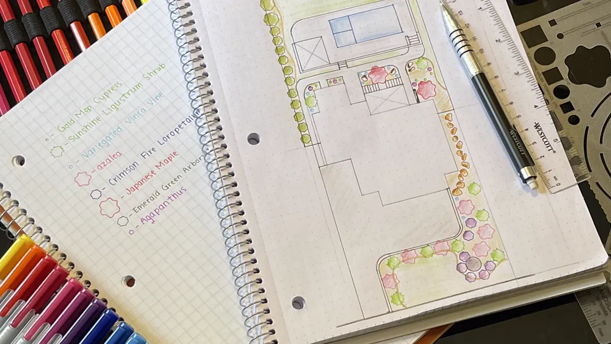 Hand-drawn landscape plan on a spiral notebook with colored pencils and a drafting template beside it