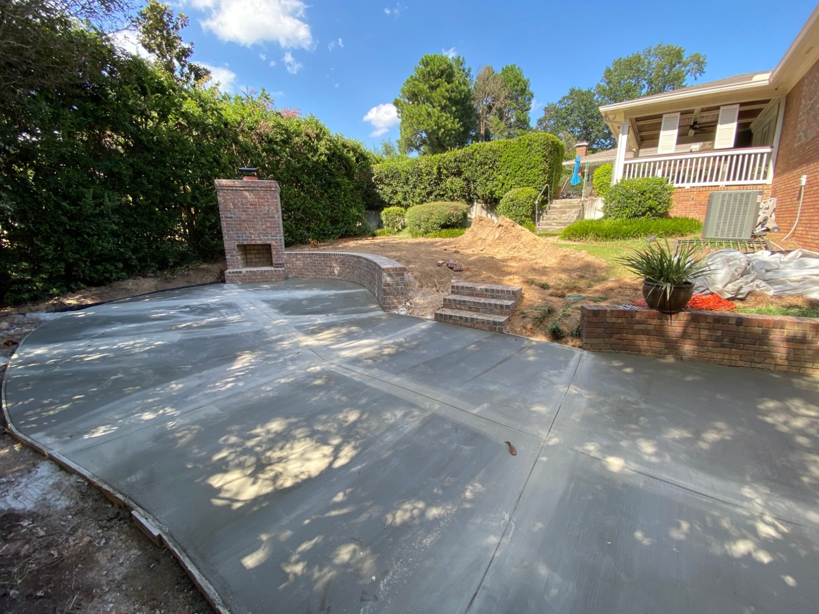 Poured concrete patio and brick fireplace under construction in a sloped back yard